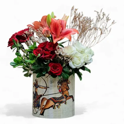 LaViola “Legend of Victory” bouquet featuring red and white roses with orange lilies in a papyrus-wrapped vase inspired by Pharaonic victory carvings of King Ramses II.