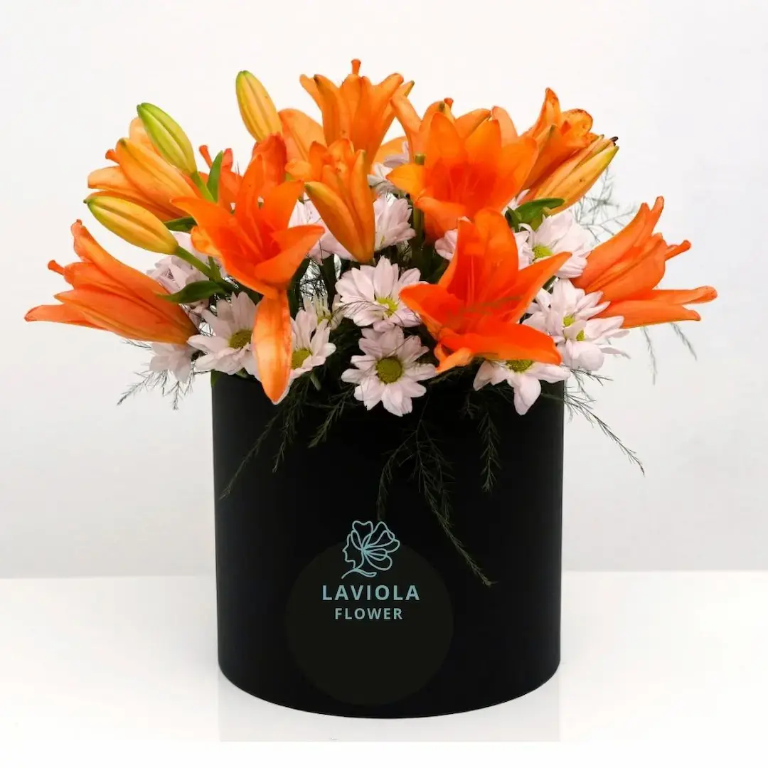 Bright flower box featuring vibrant orange lilies and white daisies arranged elegantly in a black round box by LaViola Flowers.